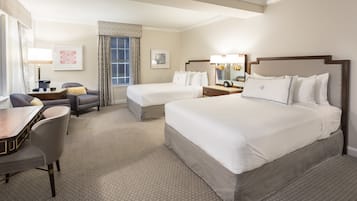 A hotel room with two beds, a desk, a chair, a dresser, and a large window with curtains.