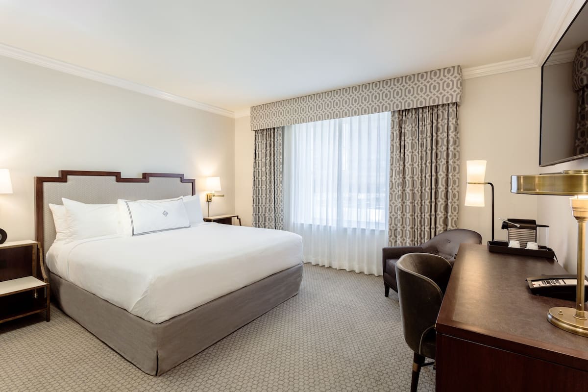 A hotel room with a large bed, a desk with a lamp, a chair, and a television.