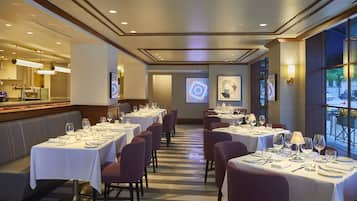 Un restaurant avec des tables dressées pour le service, un coin bar et un écran de projection fixé au mur.