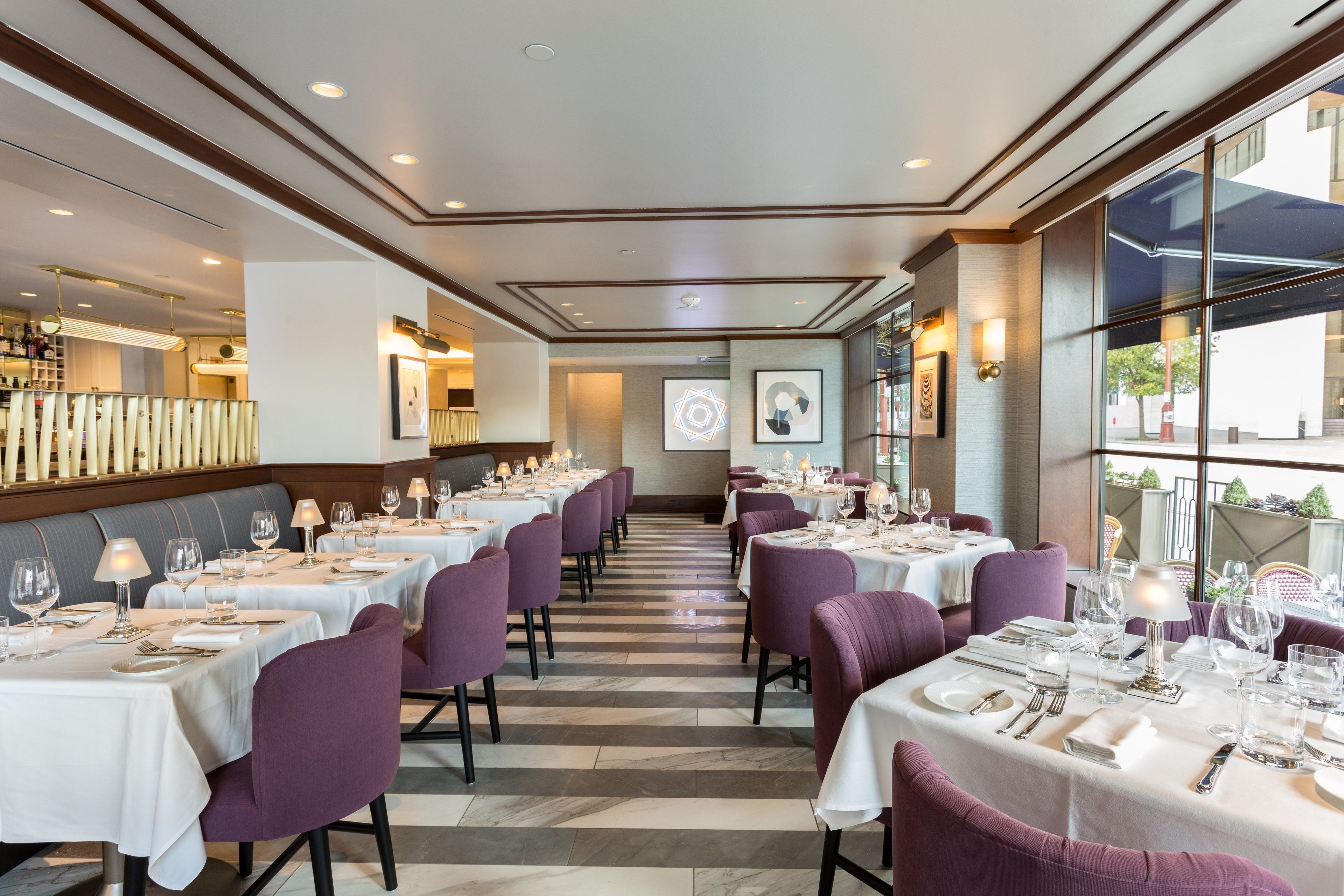 Un ristorante con diversi tavoli apparecchiati per la cena, con interni moderni, un pavimento a righe e sedie viola.
