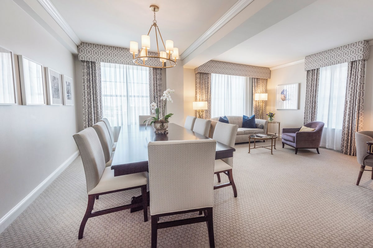 A spacious hotel room with a dining area, a sofa set, and a chandelier.