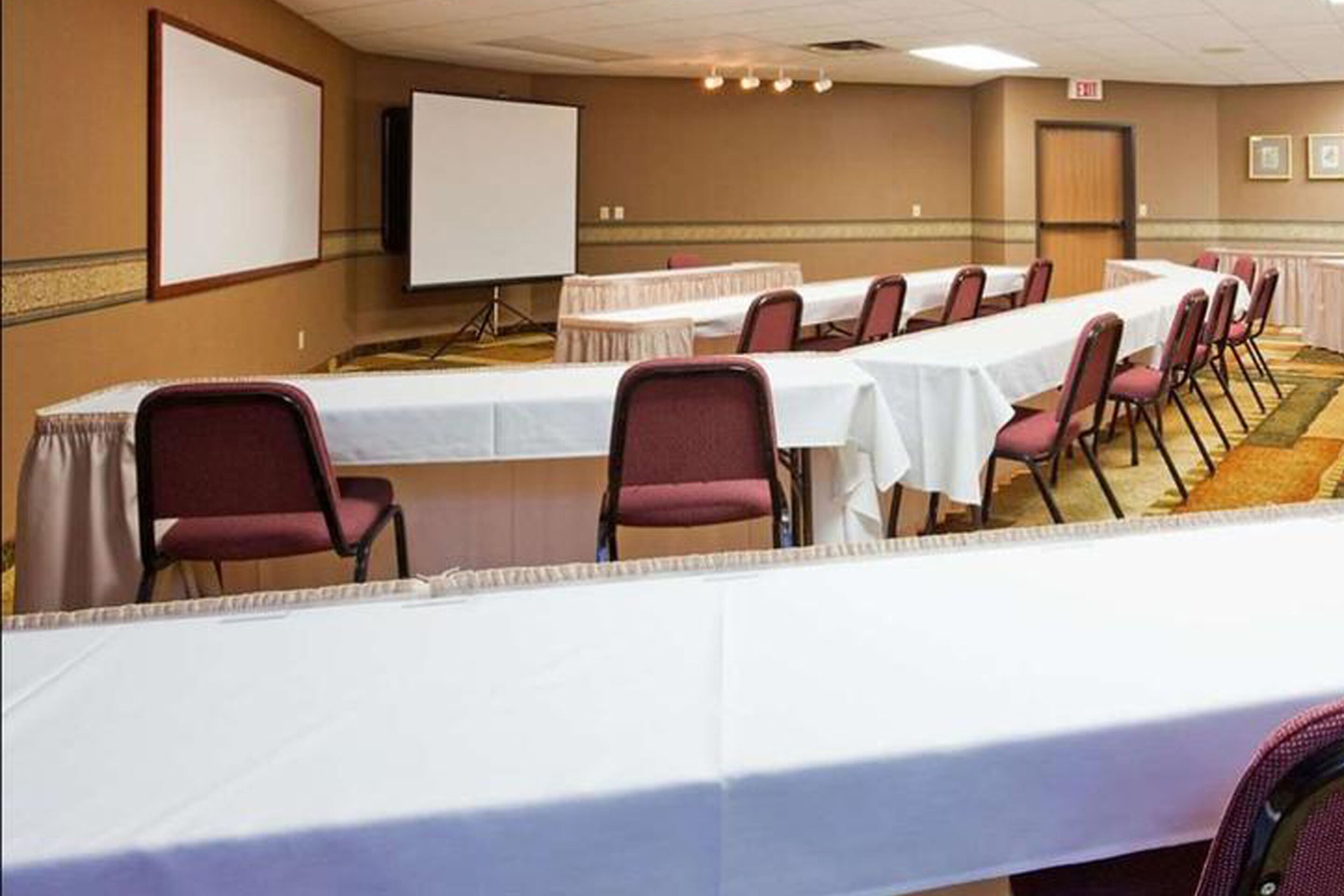 Uma sala de conferências com uma mesa comprida, cadeiras, tela de projetor e quadro branco.