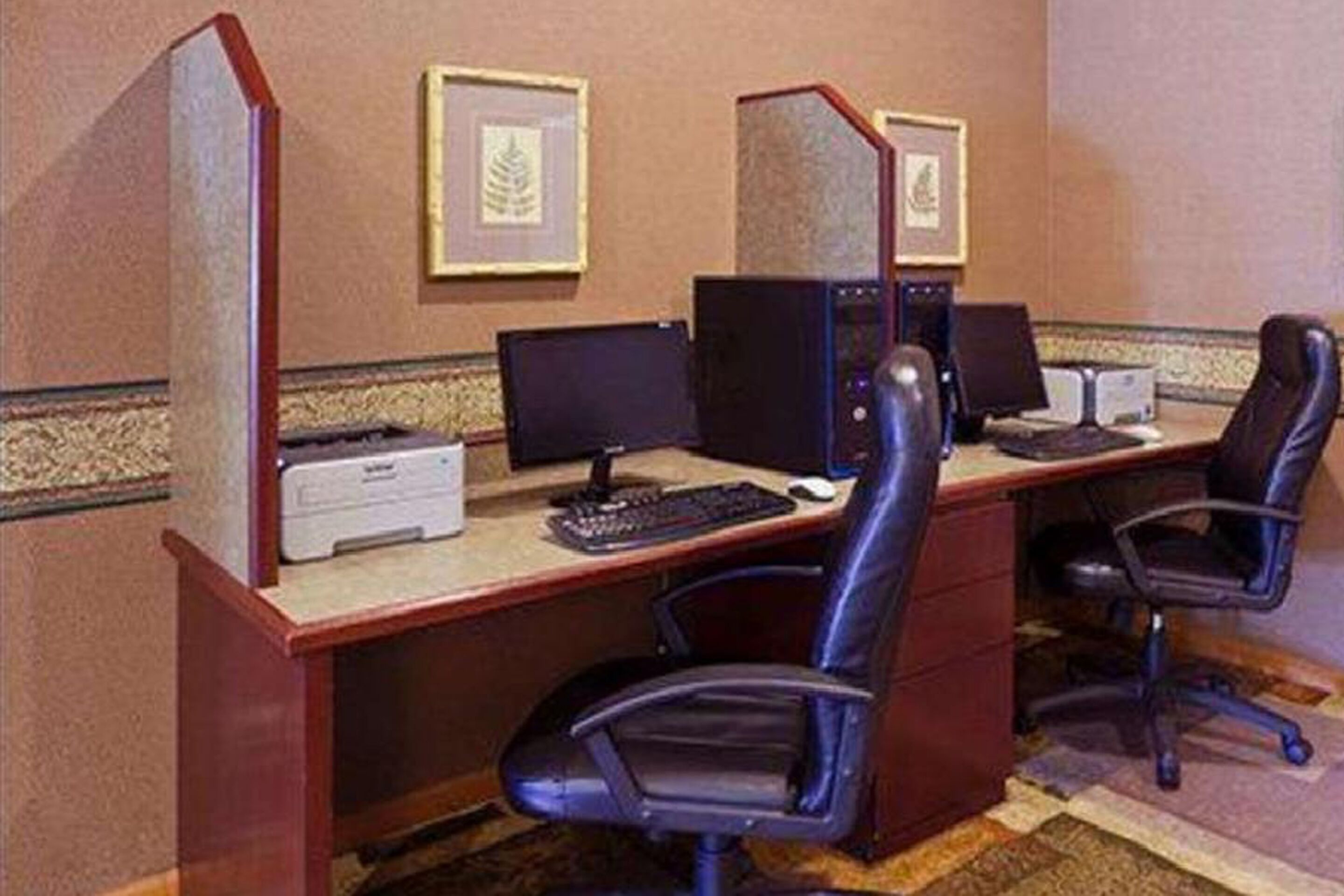 Una habitación de hotel con un escritorio, dos monitores de computadora, una impresora y dos sillas de oficina.