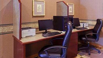 Una habitación de hotel con un escritorio, dos monitores de computadora, una impresora y dos sillas de oficina.