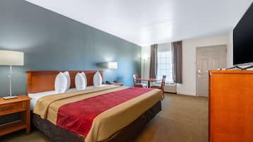 A hotel room with a large bed, a desk, a chair, a TV, and a window with curtains.