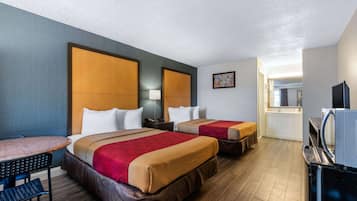 A hotel room with two beds, a desk, a chair, a TV, and a bathroom visible in the background.