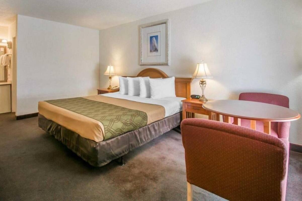 A hotel room with a bed, bedside tables, a desk, a chair, and a picture on the wall.