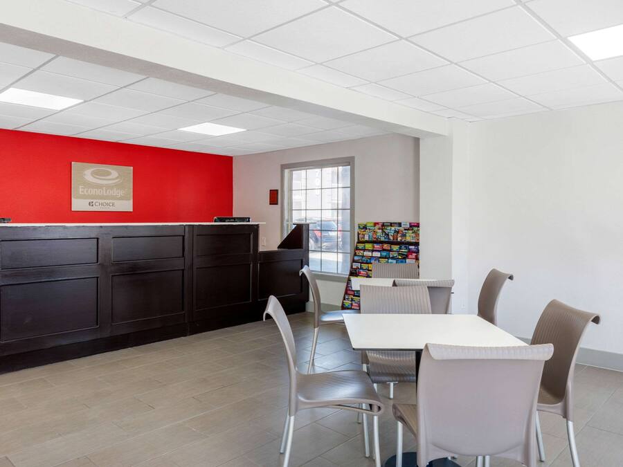 A reception area with a red wall, a dark reception desk, and a window. There are four chairs and a table in the foreground.
