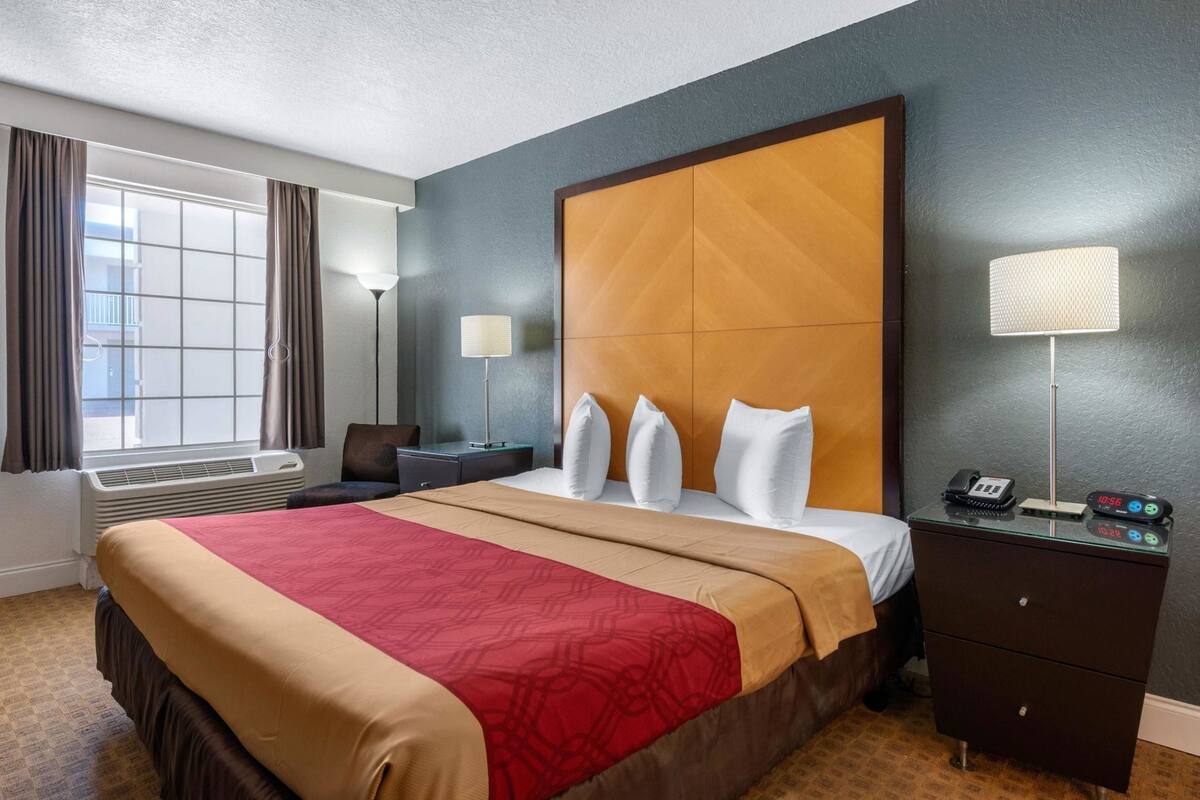 A hotel room with a large bed, bedside tables, a desk, a lamp, and a clock.