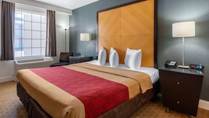 Une chambre d’hôtel avec un grand lit, un bureau, une chaise, une lampe et une table de chevet avec un téléphone et une horloge.