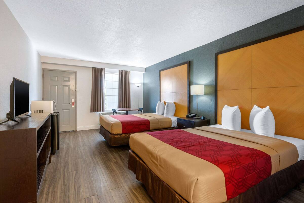 A hotel room with two beds, a desk, a TV, and a door.