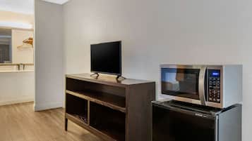 A modern kitchen with a flat-screen TV on a wooden stand, a built-in microwave, and a white countertop.