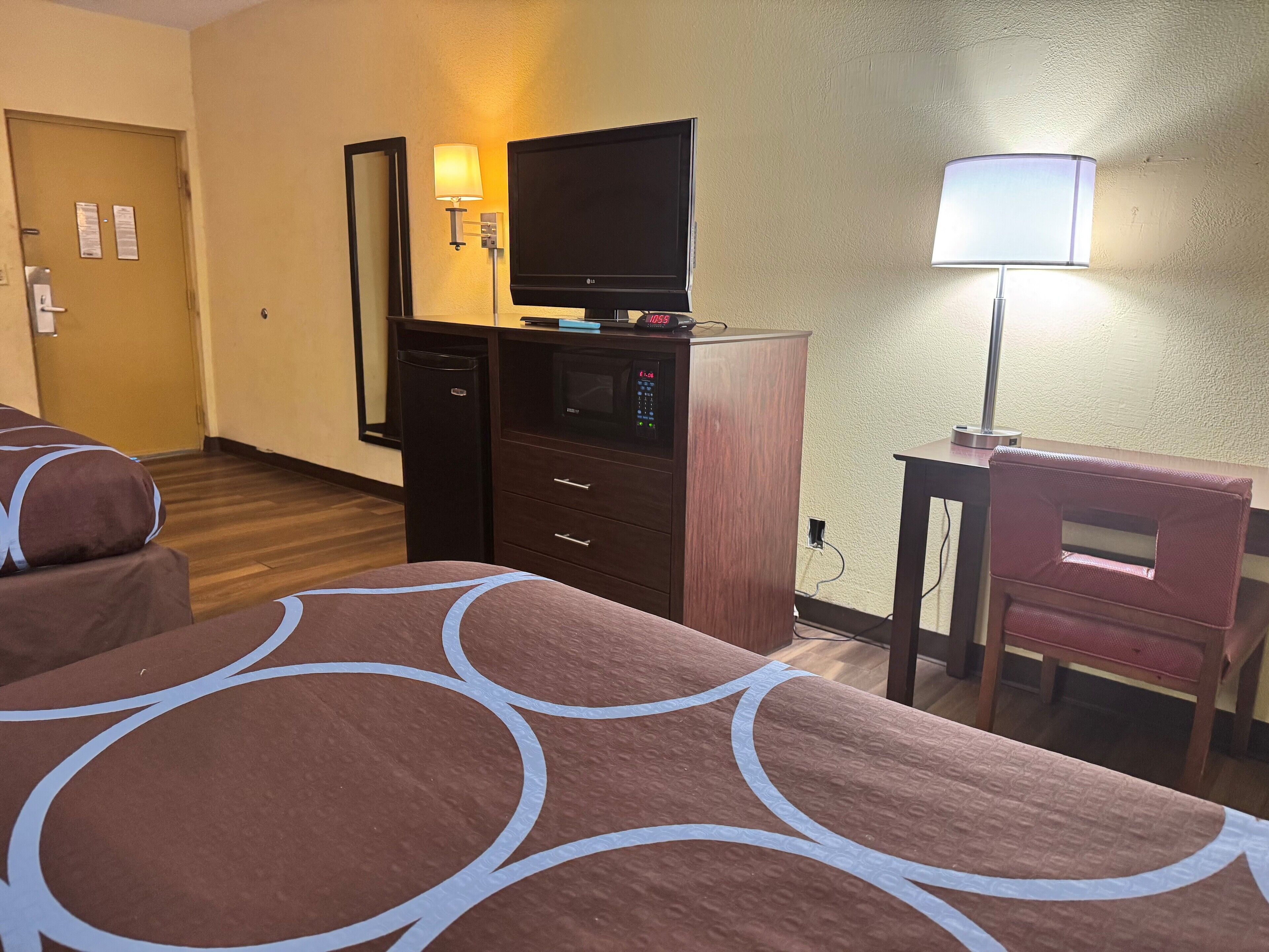 Una habitación de hotel con dos camas, un escritorio, una silla, un televisor y una lámpara.