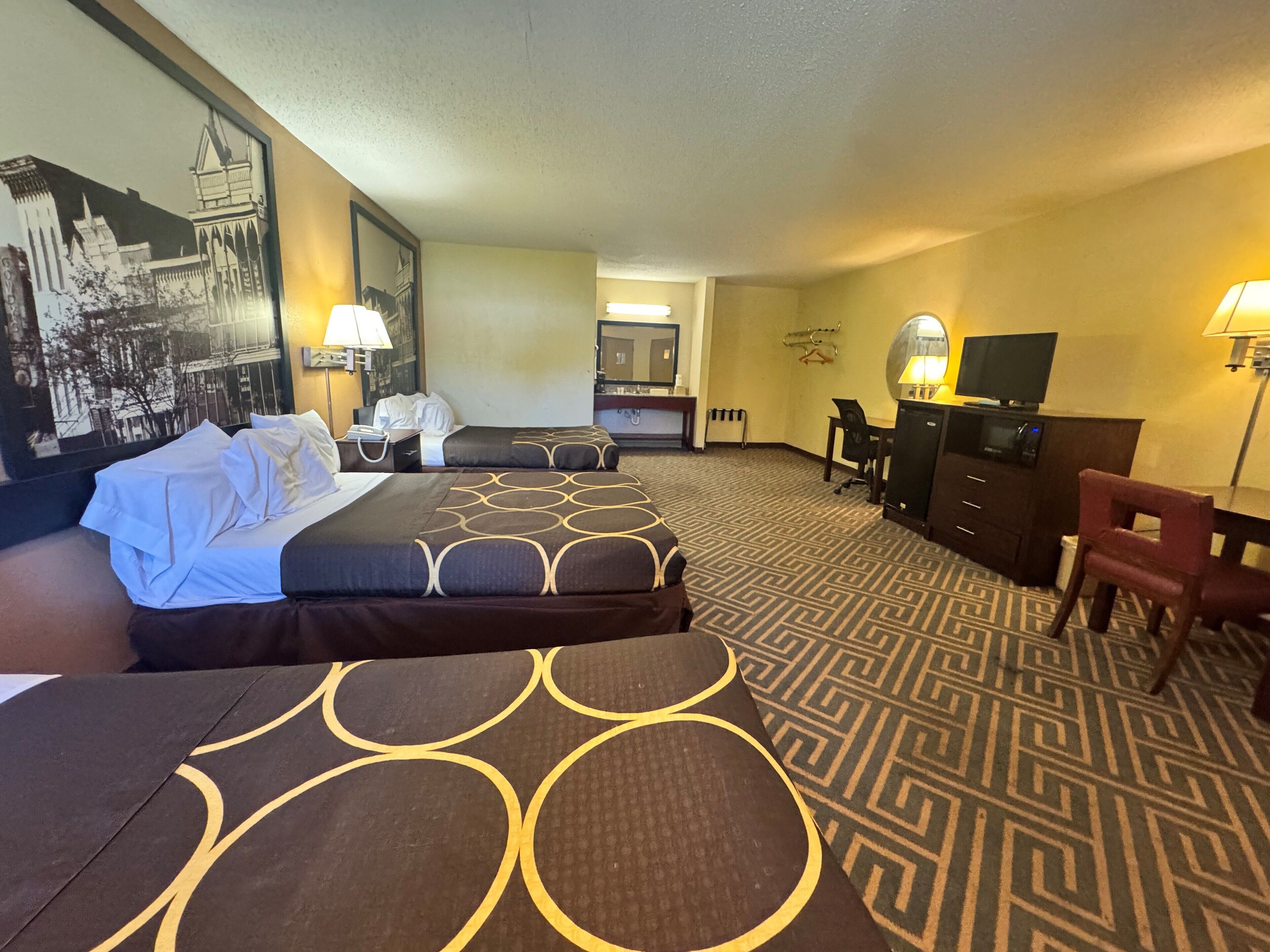 A hotel room with two beds, a desk, a chair, a television, and a large framed picture on the wall.