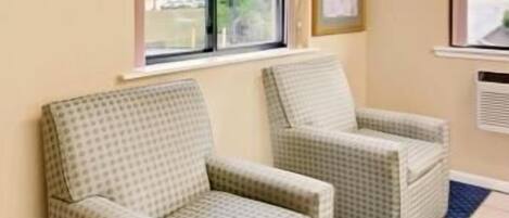 A room with two patterned armchairs, a window with a view of the outdoors, and a framed certificate on the wall.