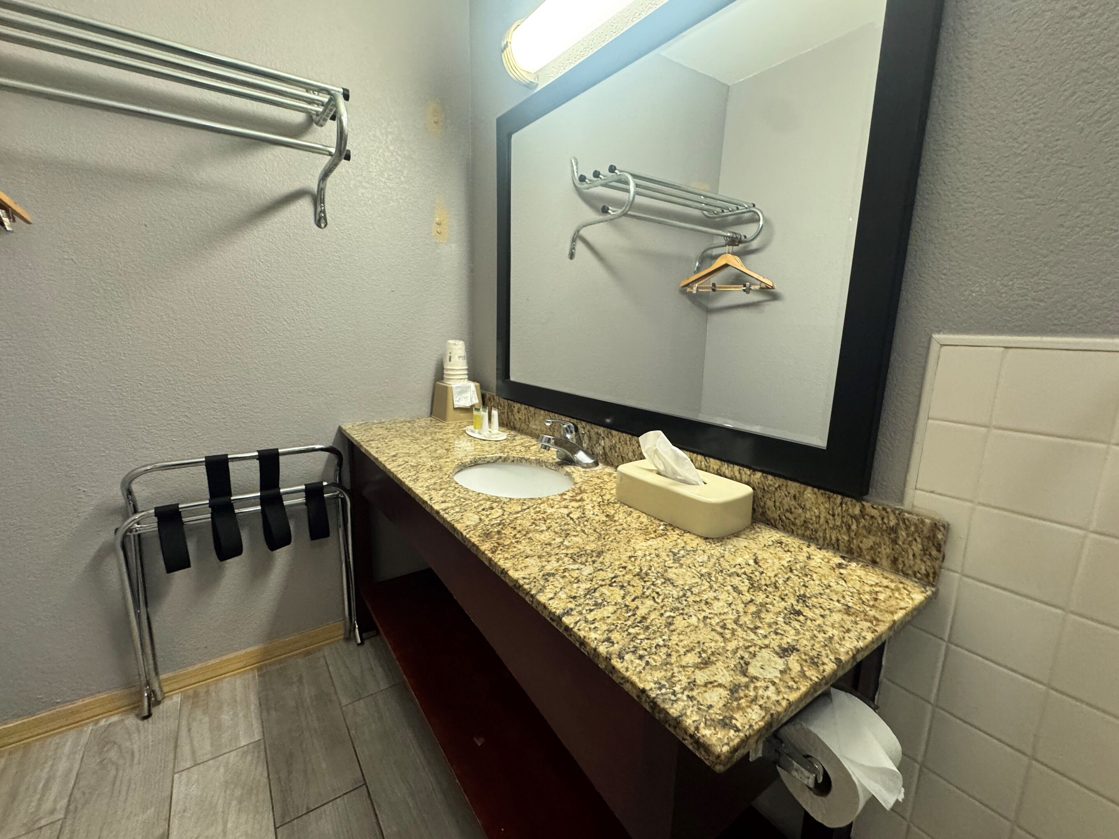 A bathroom with a granite countertop sink, a mirror, a towel rack, a hand dryer, and a toilet paper holder.