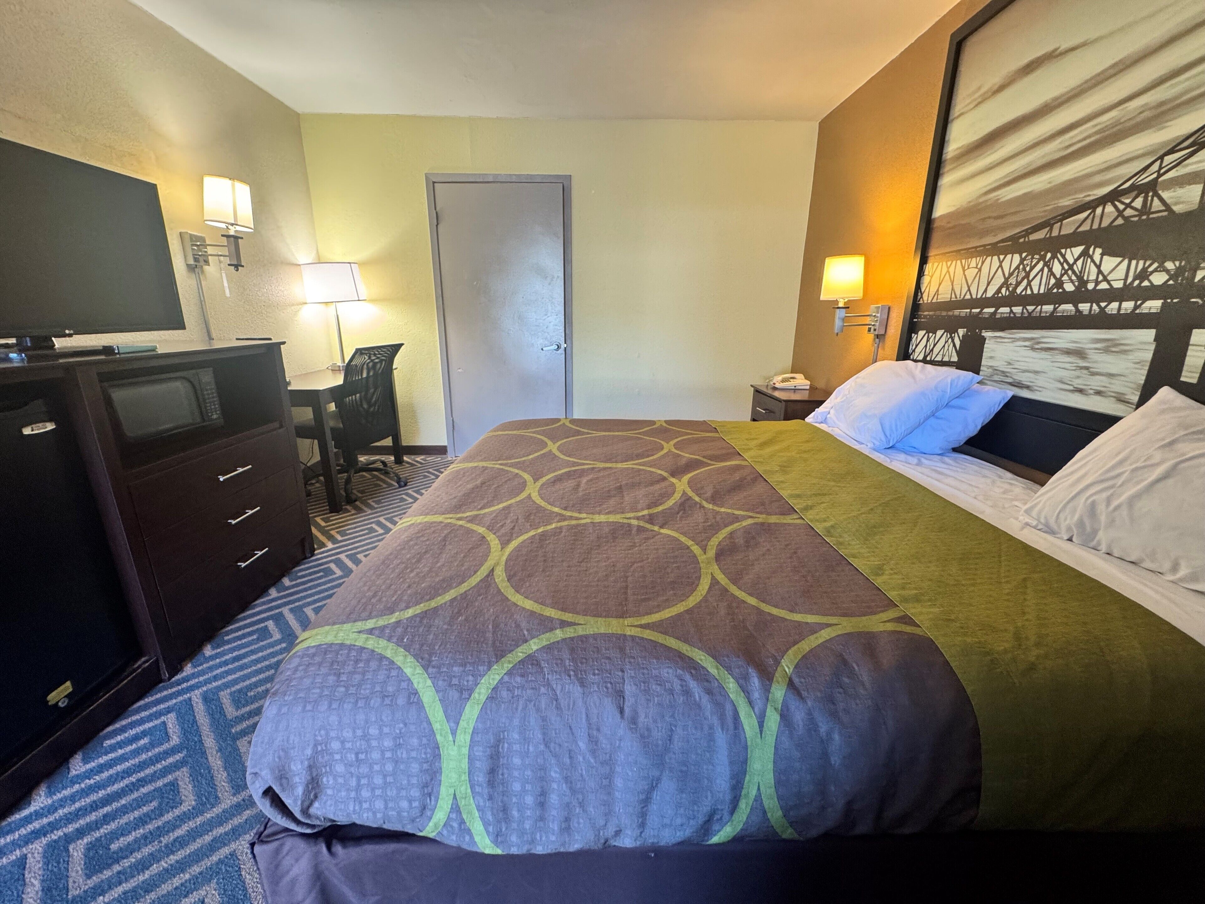 A hotel room with a bed, a desk, a chair, a TV, and a door.