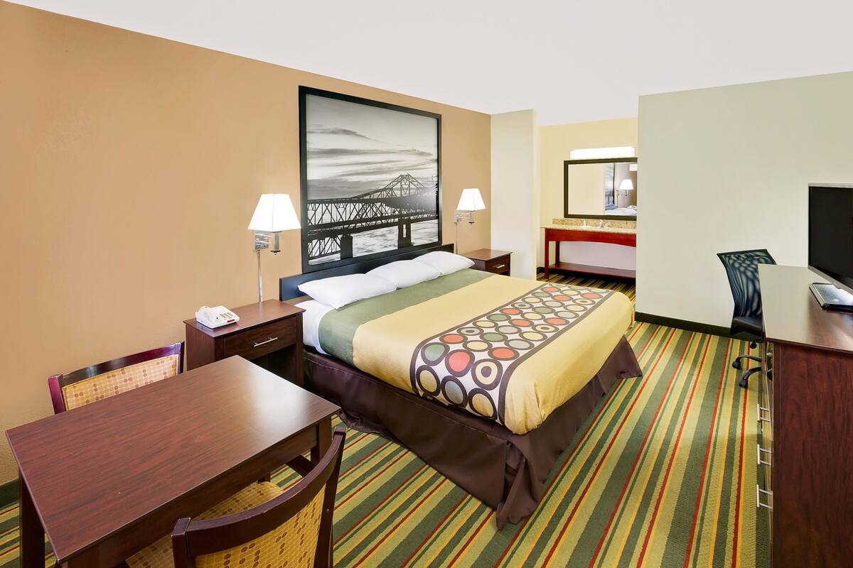 Habitación de hotel con cama, escritorio, silla, lámpara de escritorio, teléfono, televisor y un cuadro en la pared.