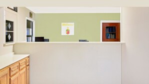 Zona de recepción con pared verde, un cartel de bienvenida, armarios de madera y una puerta.