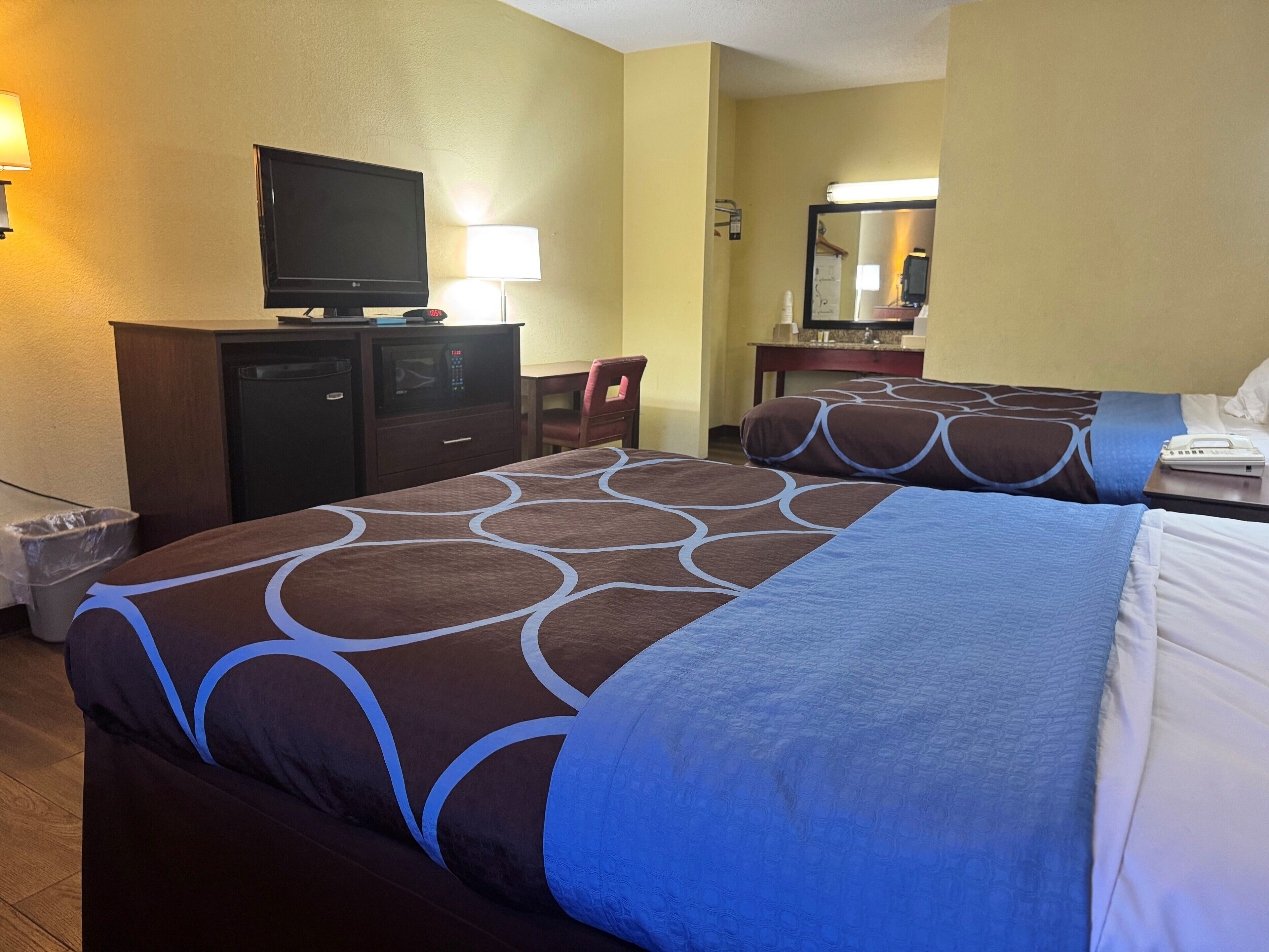 Ein Hotelzimmer mit zwei Betten, einem Schreibtisch mit Computer, einer Lampe und einem Spiegel.