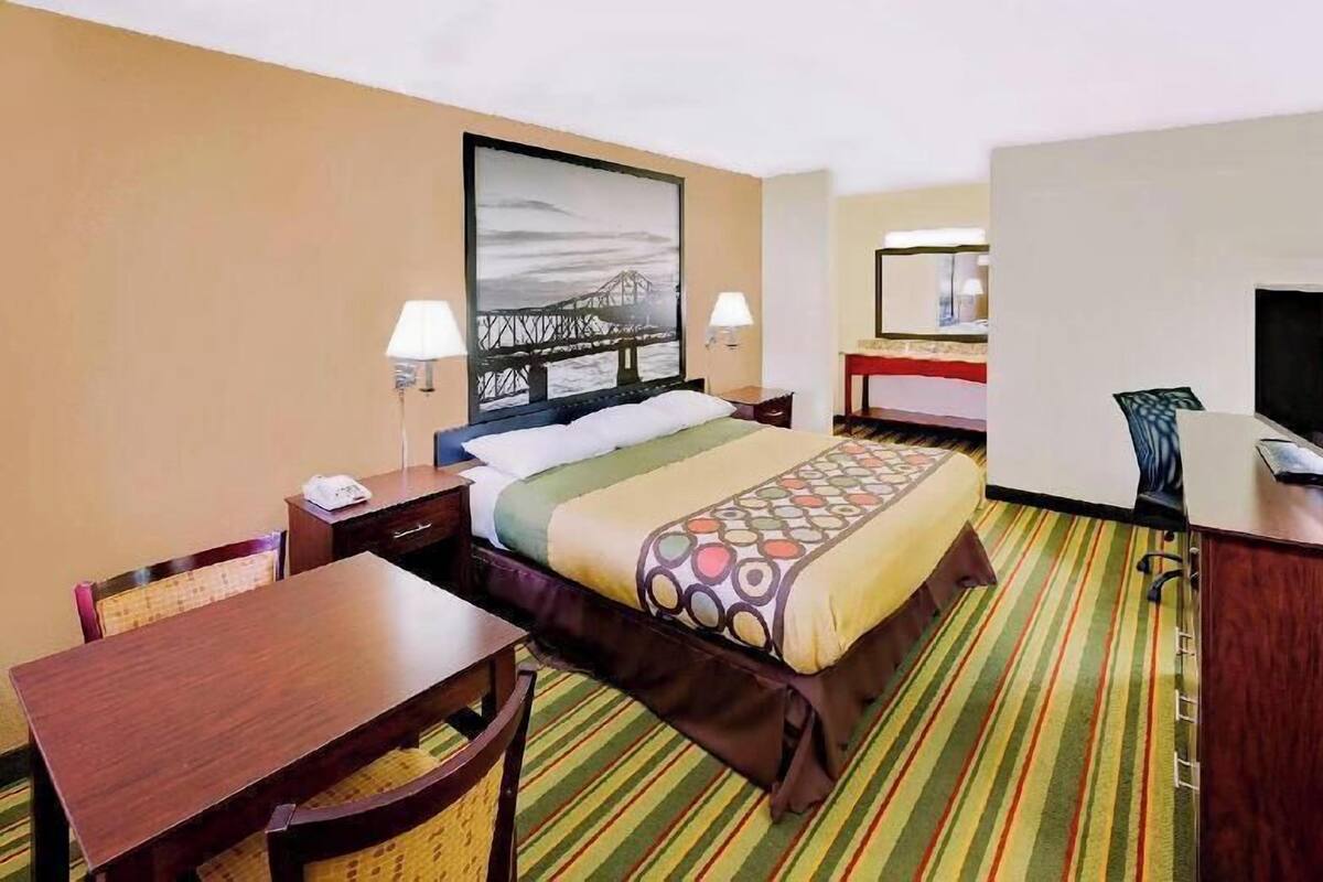 Habitación de hotel con cama, mesitas de noche, escritorio, silla, televisor y un amplio ventanal.