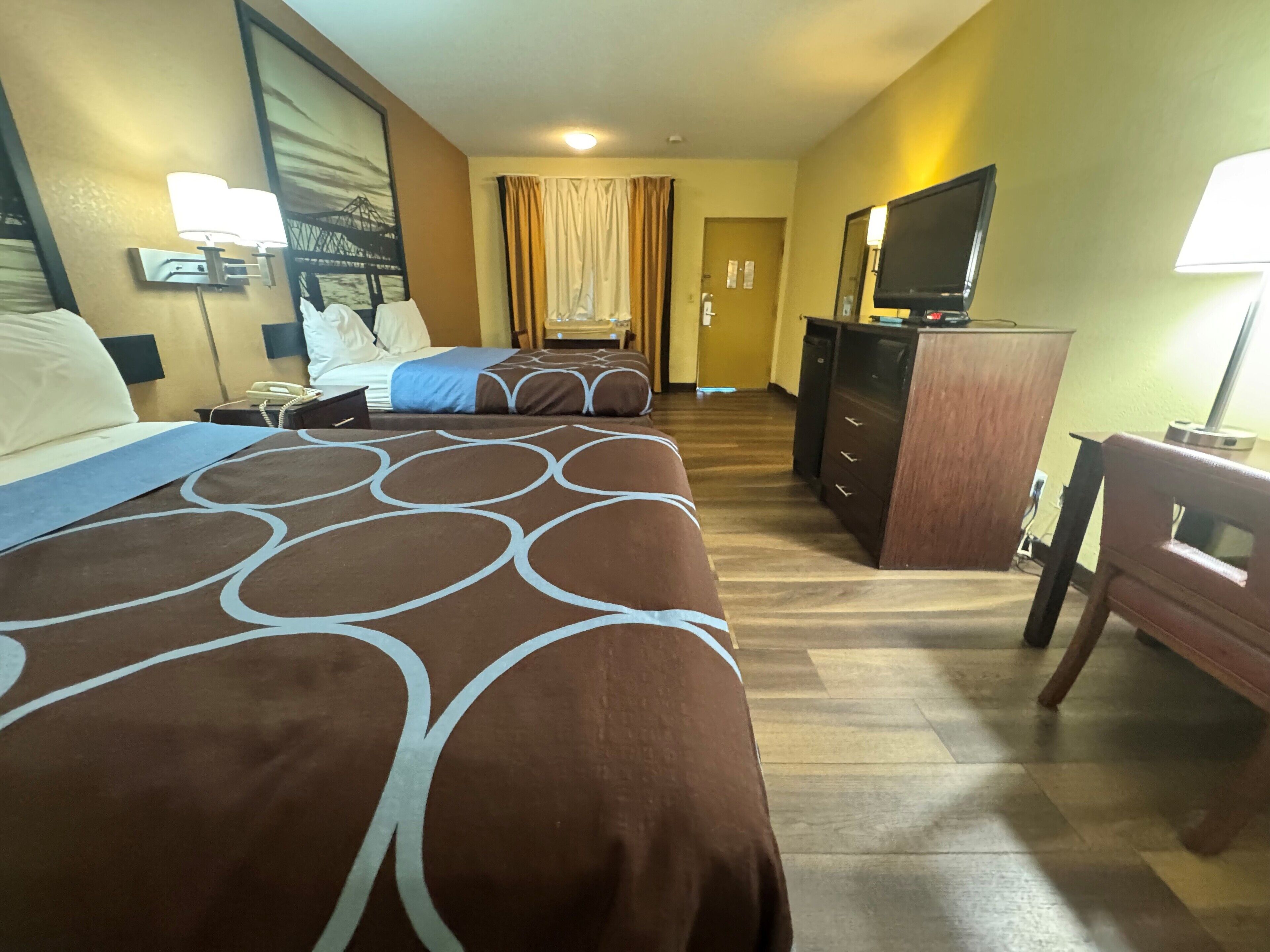 A hotel room with a large bed, a desk with a chair, a television, and a desk lamp.