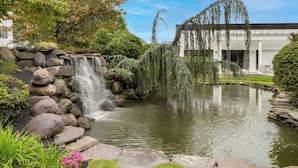 A pond with a waterfall, surrounded by rocks and greenery, and a building with a classical facade in the background. - DoubleTree Suites by Hilton Hotel Mt. Laurel (Mount Laurel)