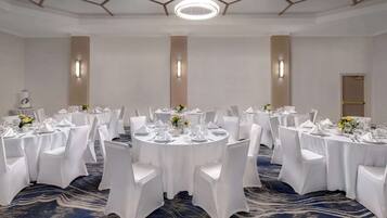 Un salón de conferencias con varias mesas redondas, cada una cubierta con mantel blanco, sillas y centros de mesa florales.