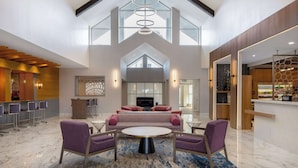 A spacious lobby with a high ceiling, a seating area with purple chairs, a central coffee table, and a bar area with a minibar. - DoubleTree Suites by Hilton Hotel Mt. Laurel (Mount Laurel)