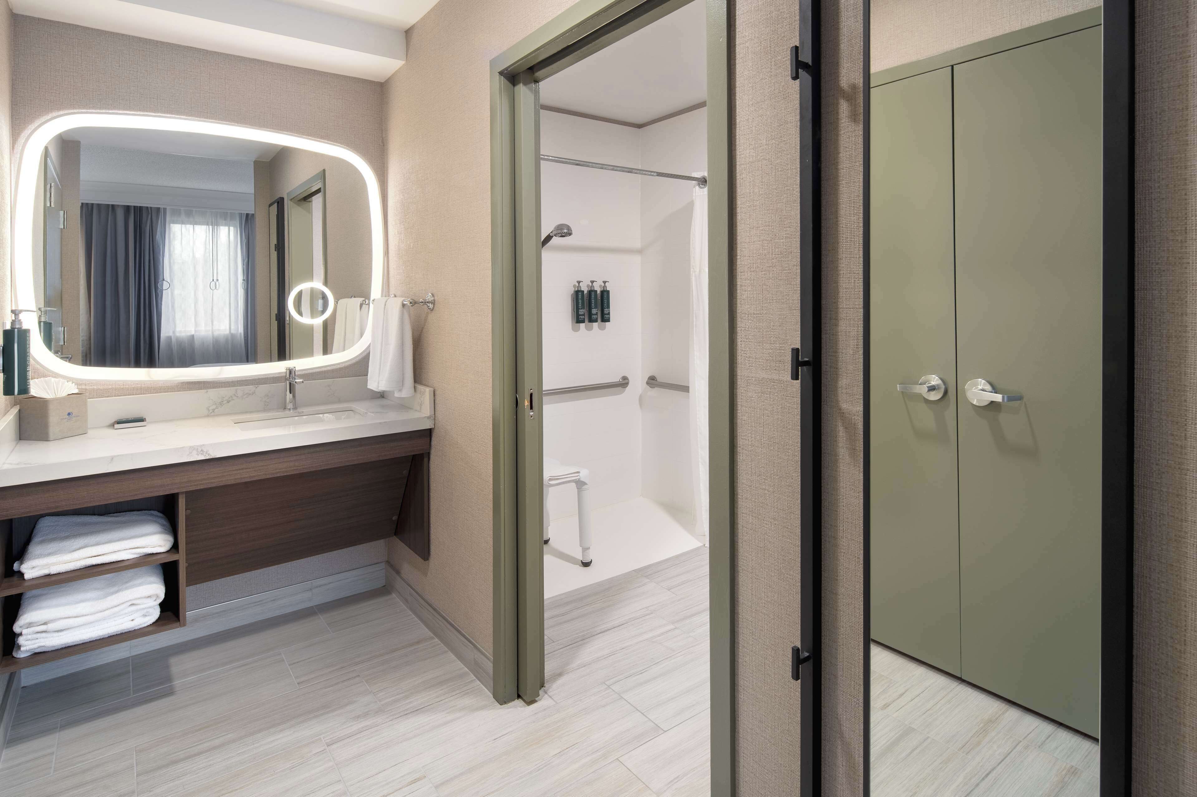 Une salle de bain moderne avec un meuble-lavabo, un grand miroir avec éclairage intégré, une douche et un placard.