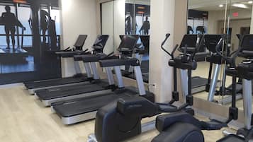 A gym with multiple treadmills, elliptical machines, and a mirrored wall.