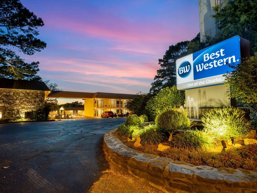 Letrero de Best Western Inn of the Ozarks, un muro de piedra de contención y un estacionamiento al anochecer.