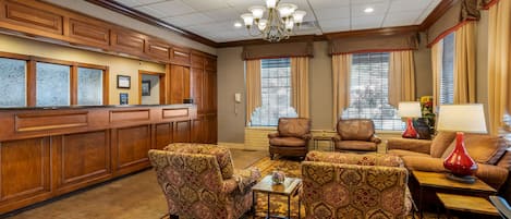 A spacious lobby with a wooden reception desk, patterned armchairs, a leather sofa, and a chandelier.