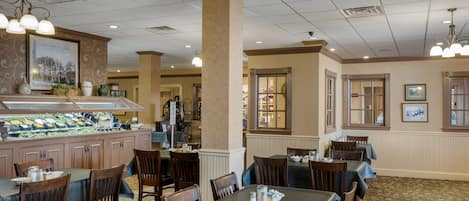 Un restaurante con varias mesas y sillas, una zona de bufé y un mostrador con exhibición de alimentos.