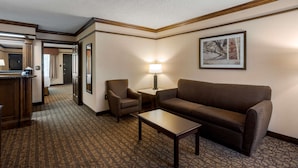 A hotel room with a brown sofa, a small table, a lamp, a chair, and a framed picture on the wall. - Best Western Inn of the Ozarks (Eureka Springs)