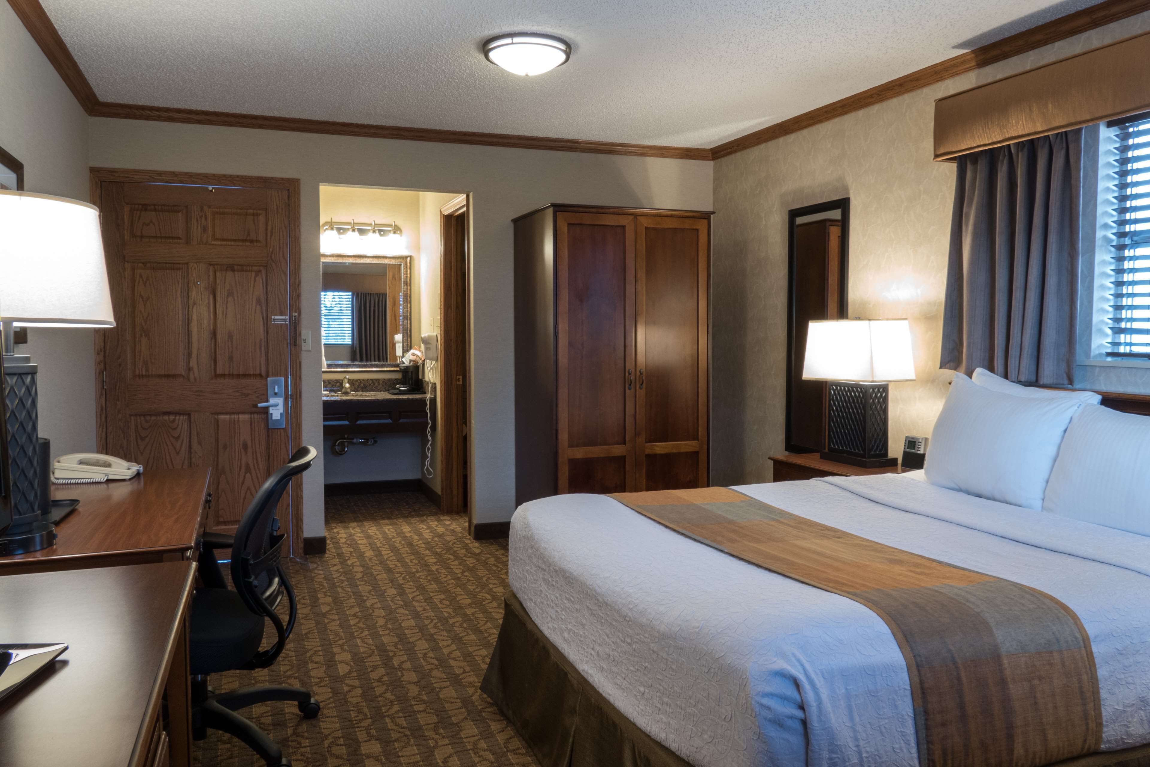 A hotel room with a bed, desk, chair, wardrobe, and bathroom.