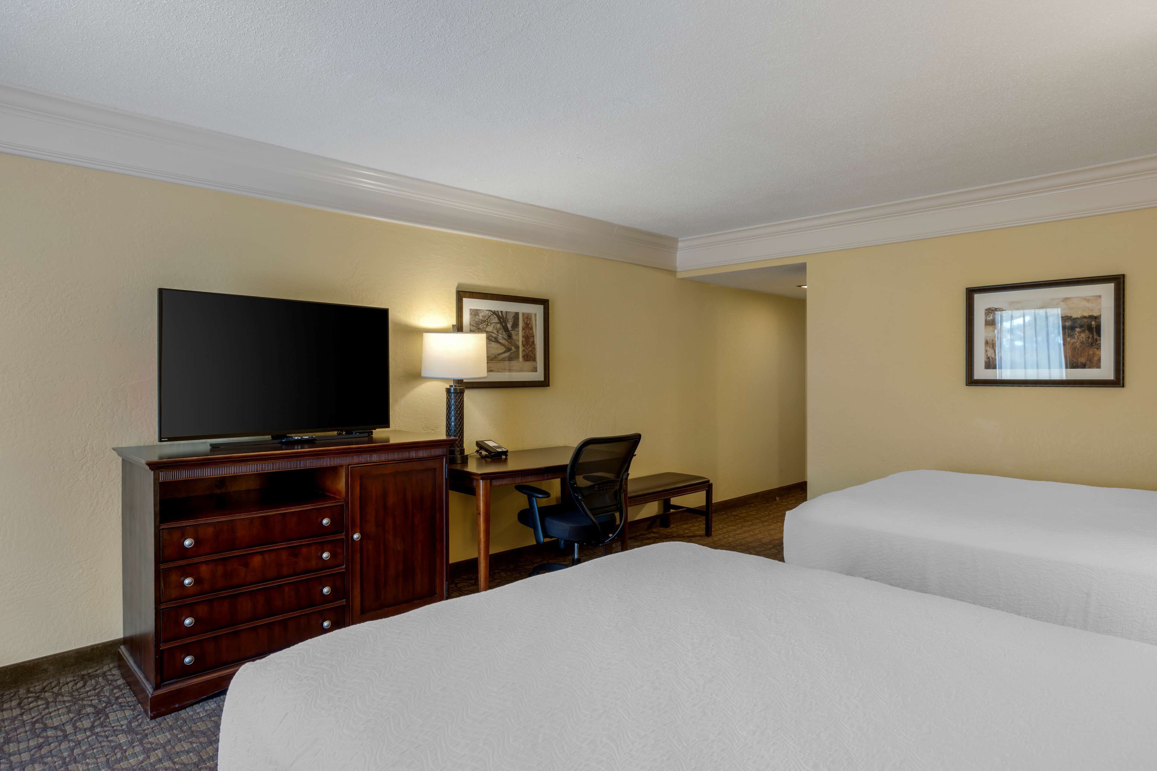Een hotelkamer met twee bedden, een bureau met stoel, een televisie en ingelijste foto's aan de muur.