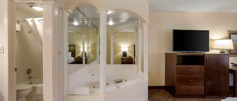 Un baño con bañera, inodoro y ducha. Hay un televisor sobre un mueble y un espejo sobre la bañera.