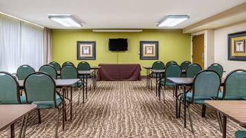 A conference room with green chairs, a long table, a television on the wall, and framed pictures on the walls.