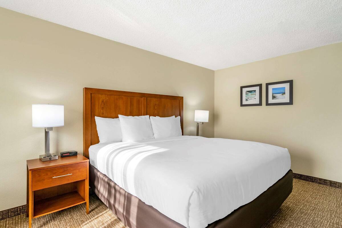 A hotel room with a large bed, a wooden nightstand, a lamp, and two framed pictures on the wall.