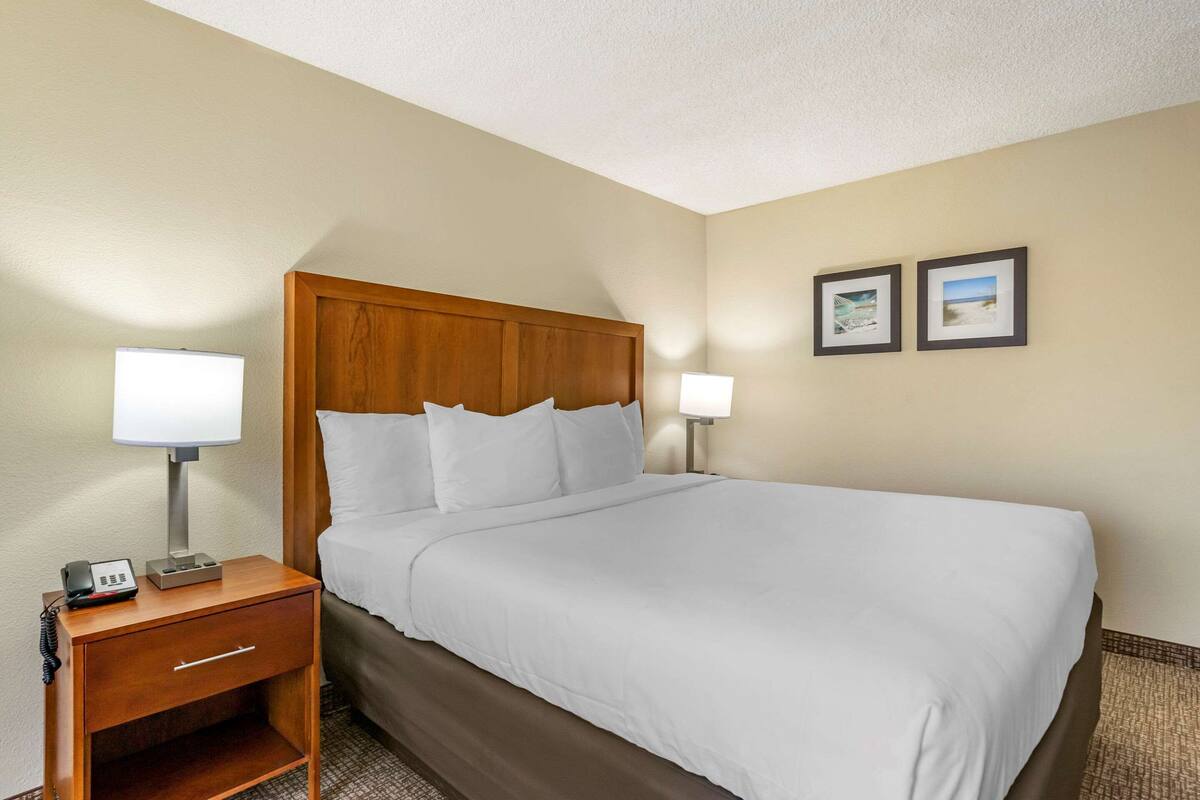 A hotel room with a wooden headboard, white bedding, a bedside table with a lamp, and two framed pictures on the wall.