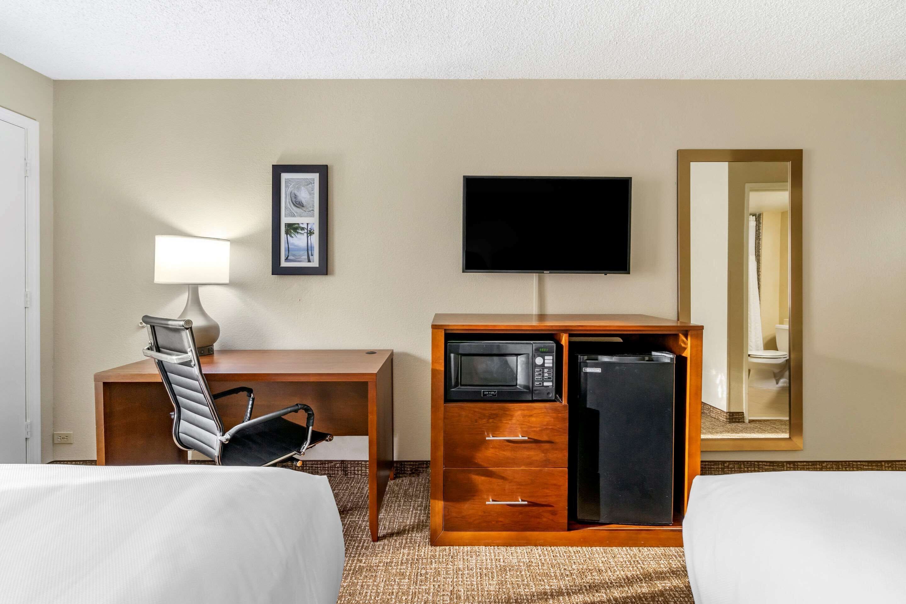 A hotel room with a bed, a desk, a chair, a television, a microwave, and a refrigerator.