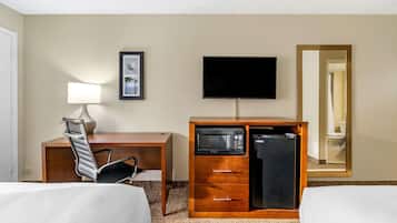 Een hotelkamer met een bed, een bureau, een stoel, een televisie, een magnetron en een koelkast.
