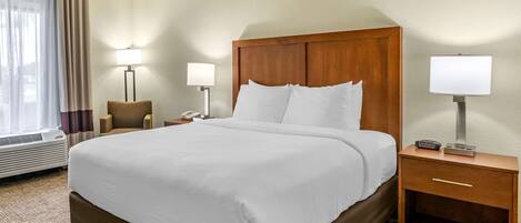 A hotel room with a large bed, two bedside tables with lamps, a chair, and a desk.