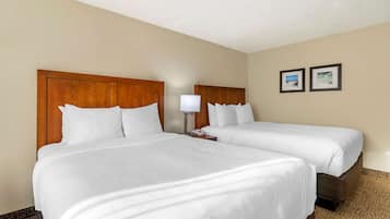 A hotel room with two beds, a wooden headboard, a bedside table with a lamp, and two framed pictures on the wall.