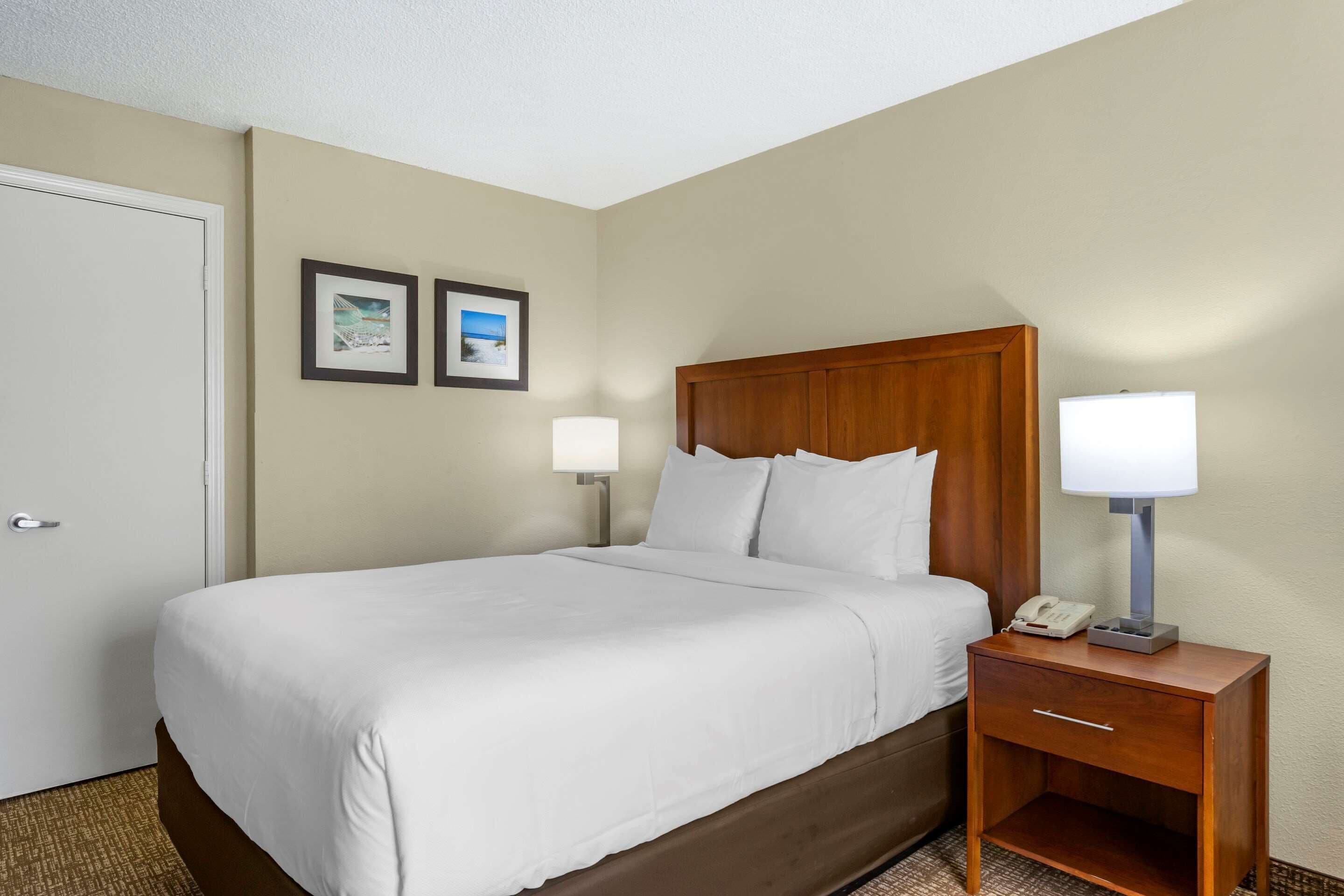A hotel room with a single bed, a wooden headboard, two bedside lamps, a nightstand with a phone, and two framed pictures on the wall.