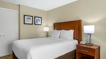 A hotel room with a single bed, a wooden headboard, two bedside lamps, a nightstand with a phone, and two framed pictures on the wall.