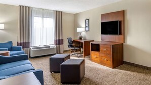 A hotel room with a sofa, a desk, an ottoman, a flat-screen TV, and a window with curtains. - Comfort Inn & Suites St. Pete - Clearwater International Airport (Clearwater)