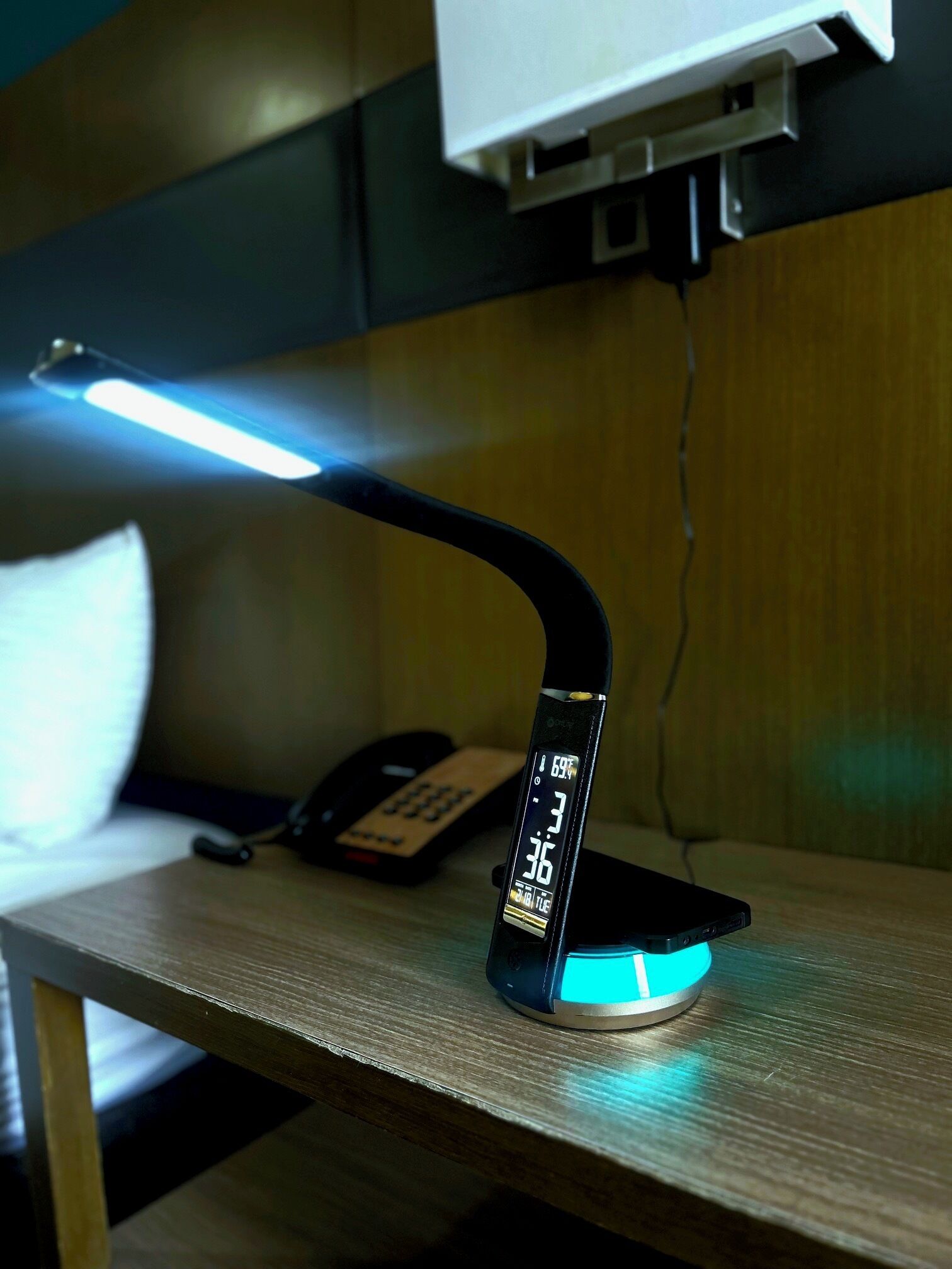 A desk with a desk lamp, a phone, and a digital clock displaying the time.