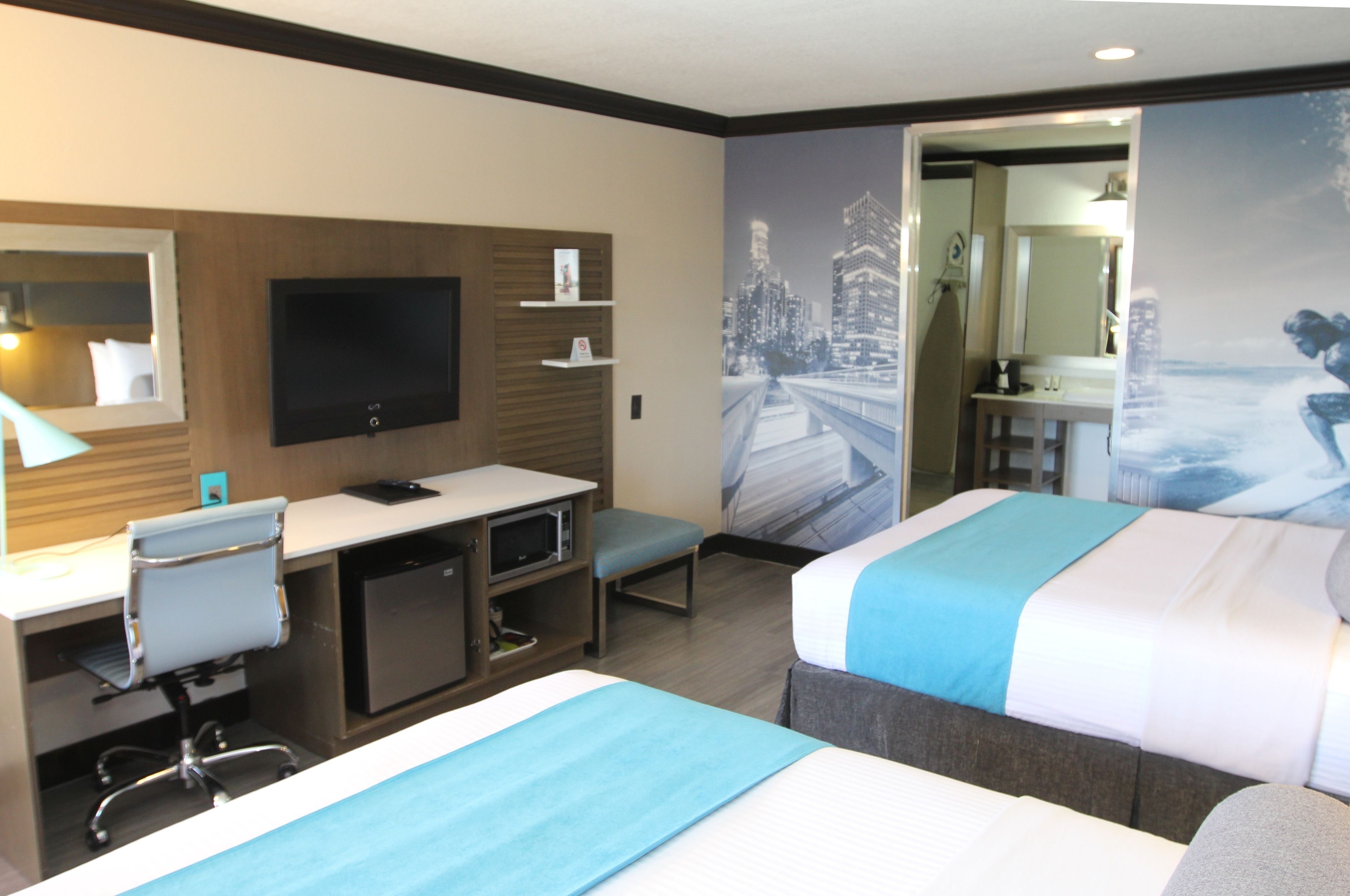 Une chambre d’hôtel avec deux lits, un bureau avec un ordinateur, une télévision et une salle de bain visible à travers une porte ouverte.